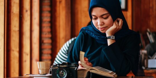 woman sitting beside table reading book