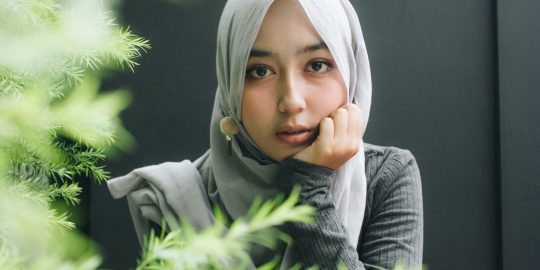 woman wearing gray long-sleeved top and gray hijab right hand on cheek